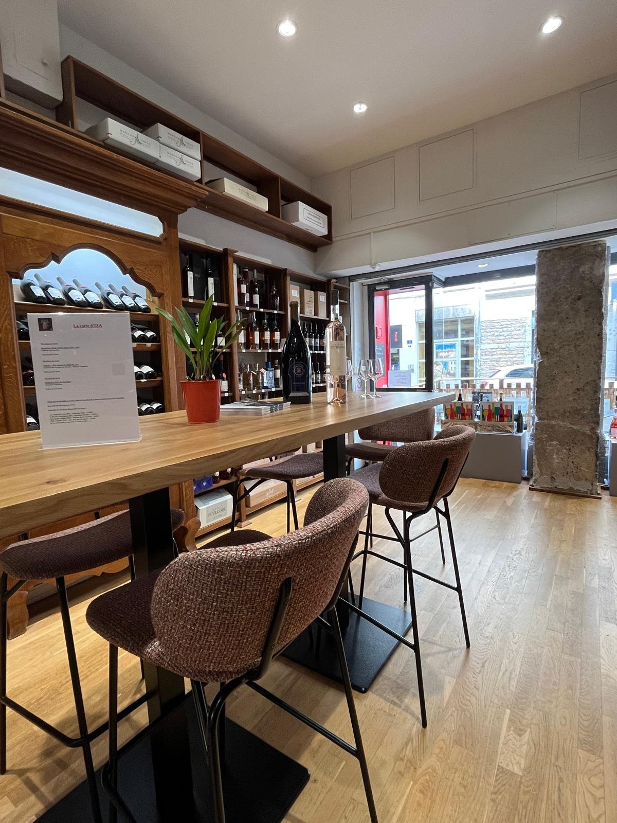 Grande table haute en bois entourée de chaises capitonnées, verres et bouteilles disposés pour une dégustation